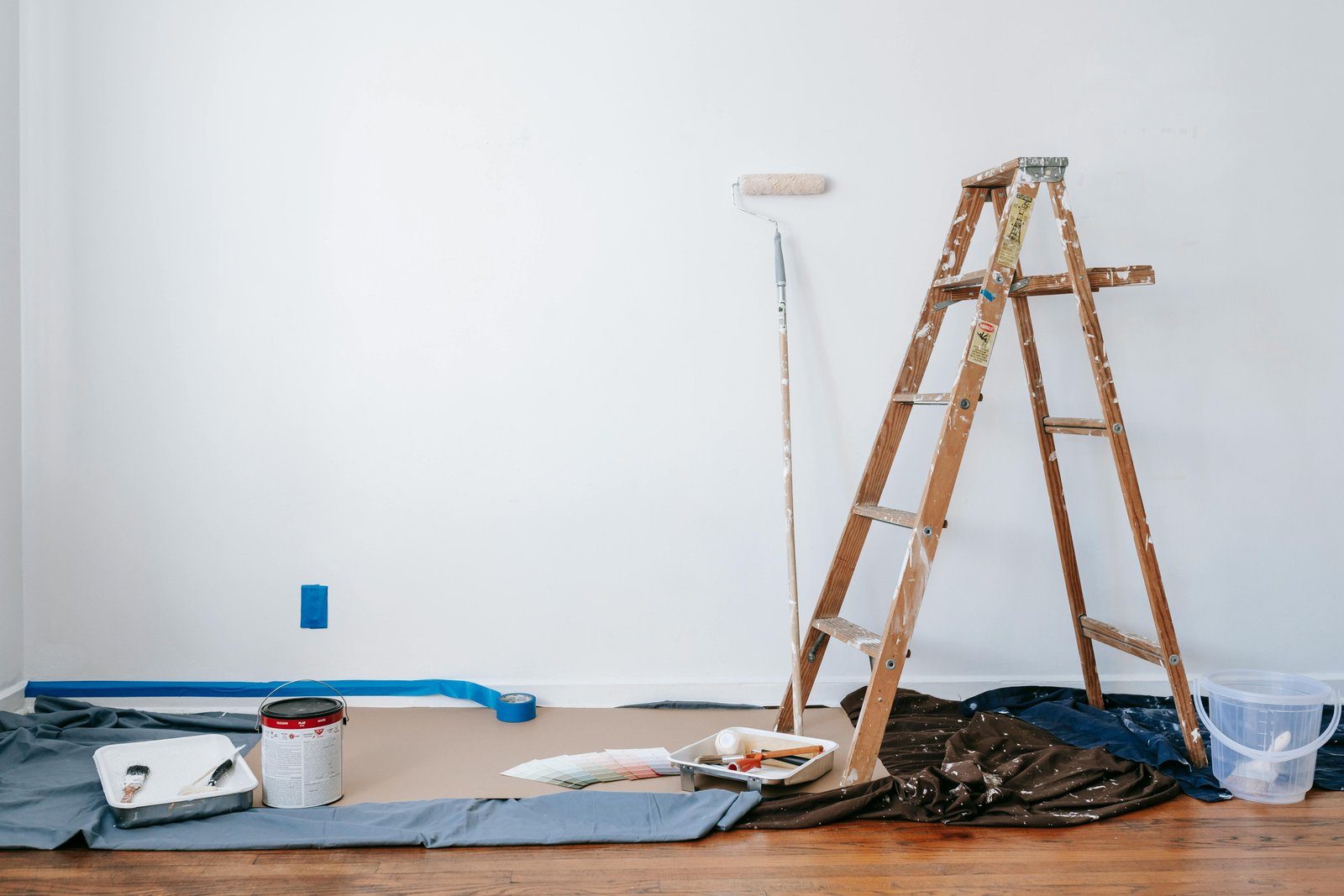Home A room prepared for renovation with a ladder, paint supplies, and drop cloth.