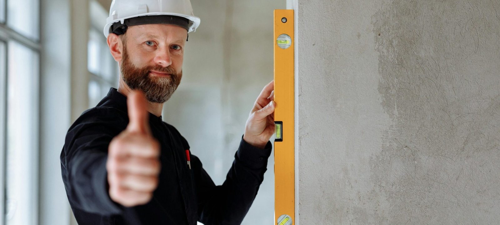 pexels photo 8482823 8482823 Professional construction worker with hard hat and spirit level giving thumbs up indoors.